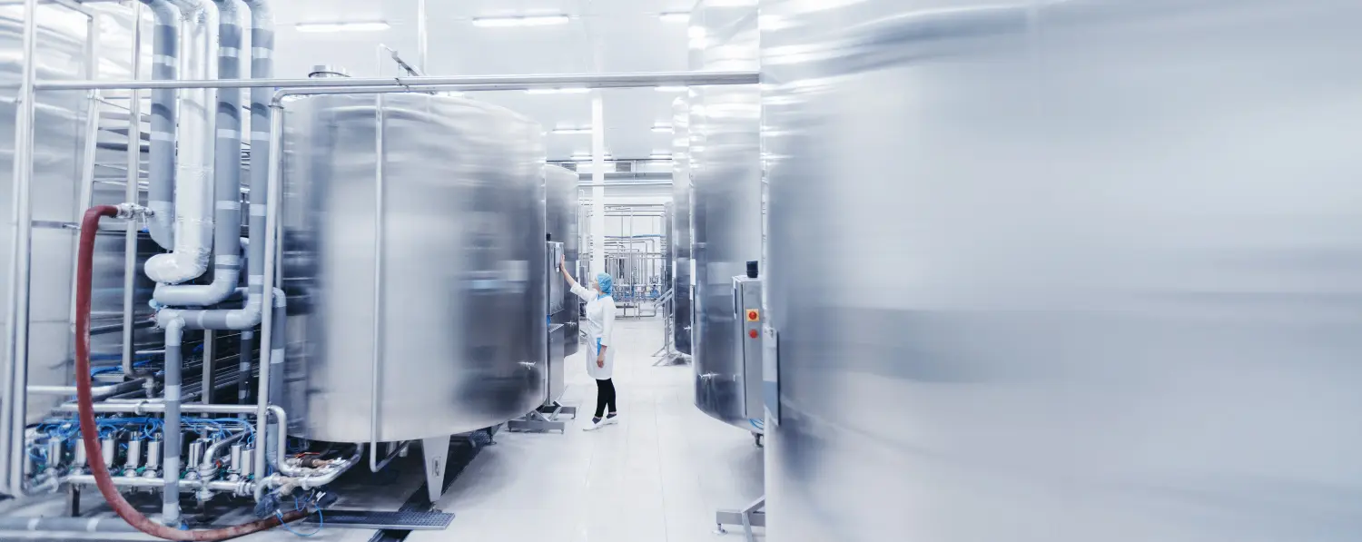 Energieberatung - Energieeinkaufsmanagement - Eine weibliche Ingenieurin in Uniform bedient ein Prozesssteuerfeld an einer Produktionslinie in einer Lebensmittelfabrik und einen Stahltanker.